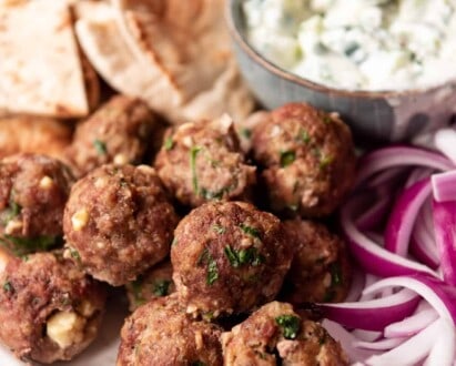 Baked Greek meatballs on a meze platter with tzatziki sauce, pita, and red onions.