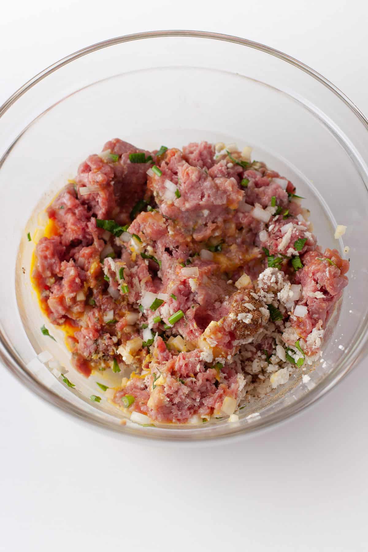 Mixing Greek meatball ingredients in a glass bowl.