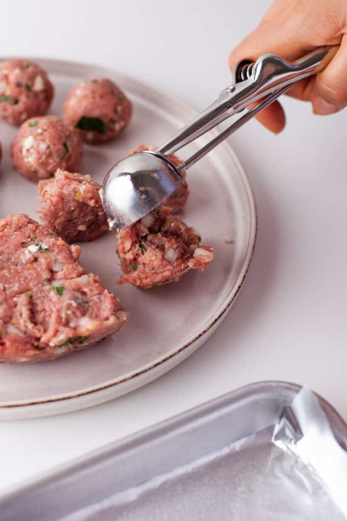 Using a small cookie scoop to measure meatballs.