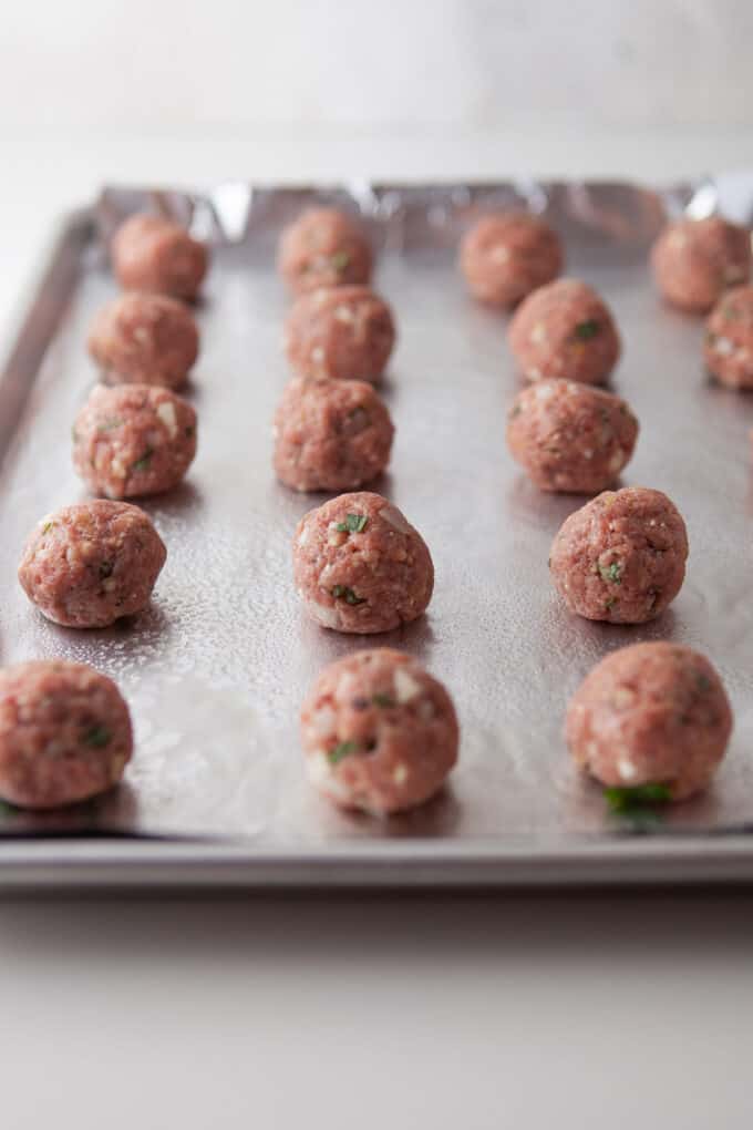 Meatballs on a baking sheet in rows ready to be baked in the oven.