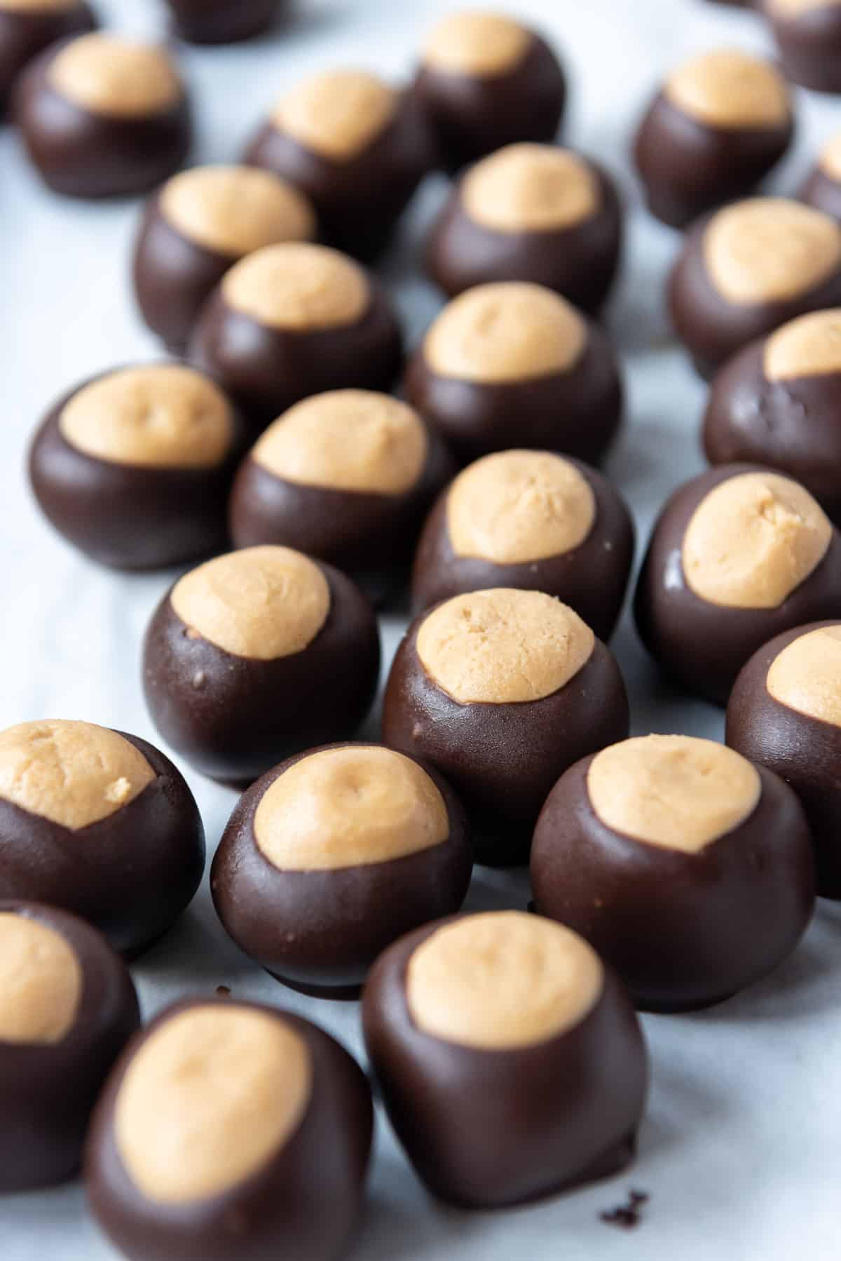 Buckeyes dipped in chocolate setting up on a baking sheet.