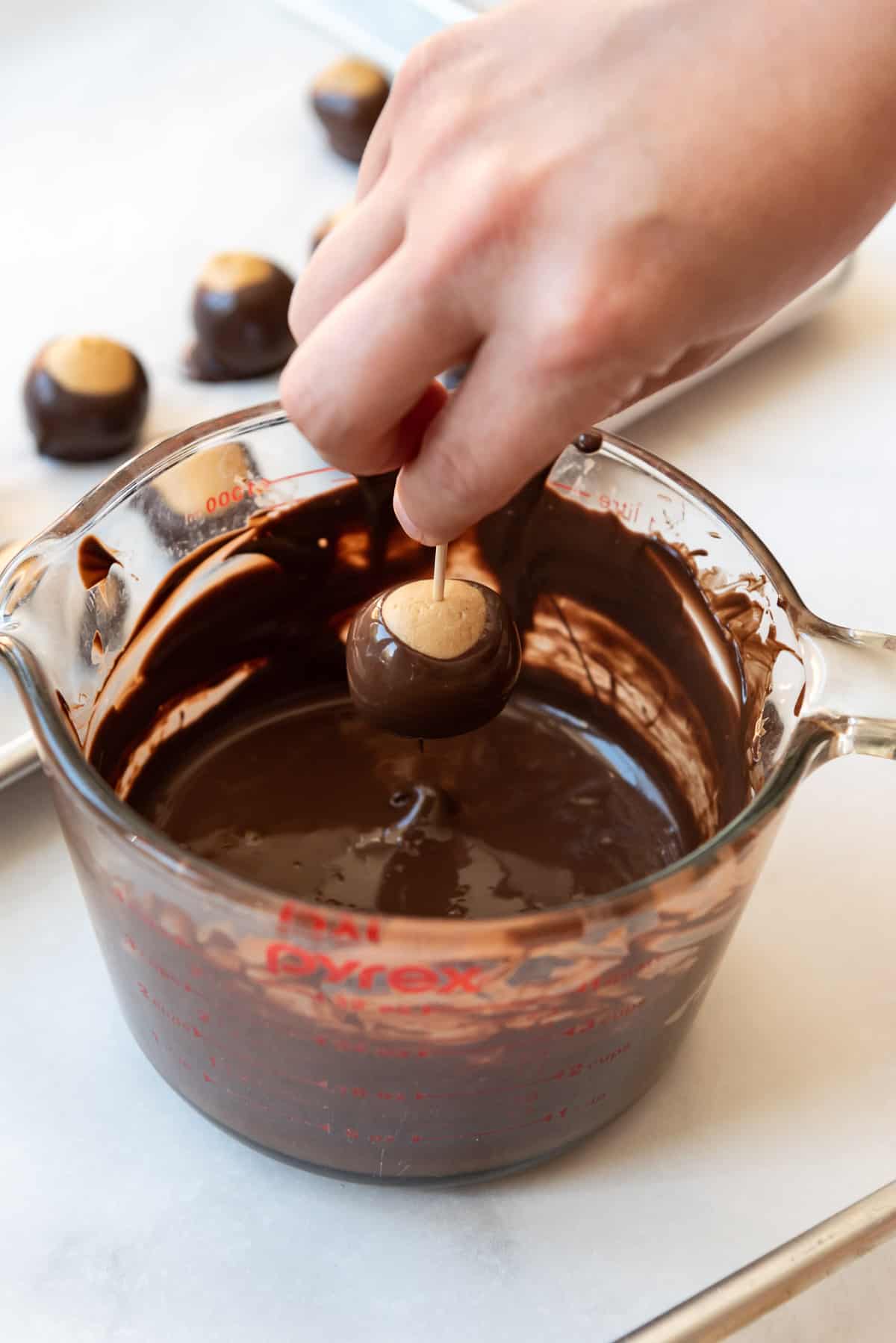 Lifting a peanut butter ball out of melted chocolate with a toothpick to make a buckeye.