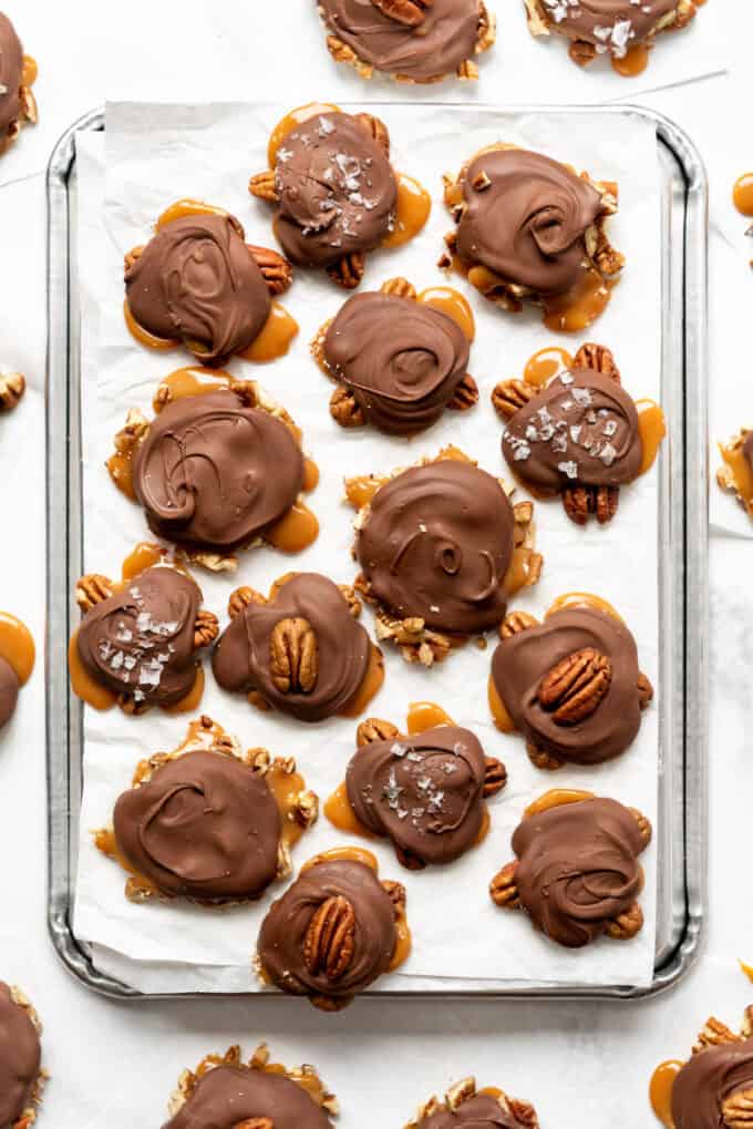 Homemade chocolate pecan turtle clusters on a baking sheet lined with parchment paper.