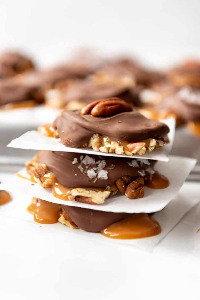 Three homemade turtles made with caramel, pecans, and chocolate stacked on top of each other.
