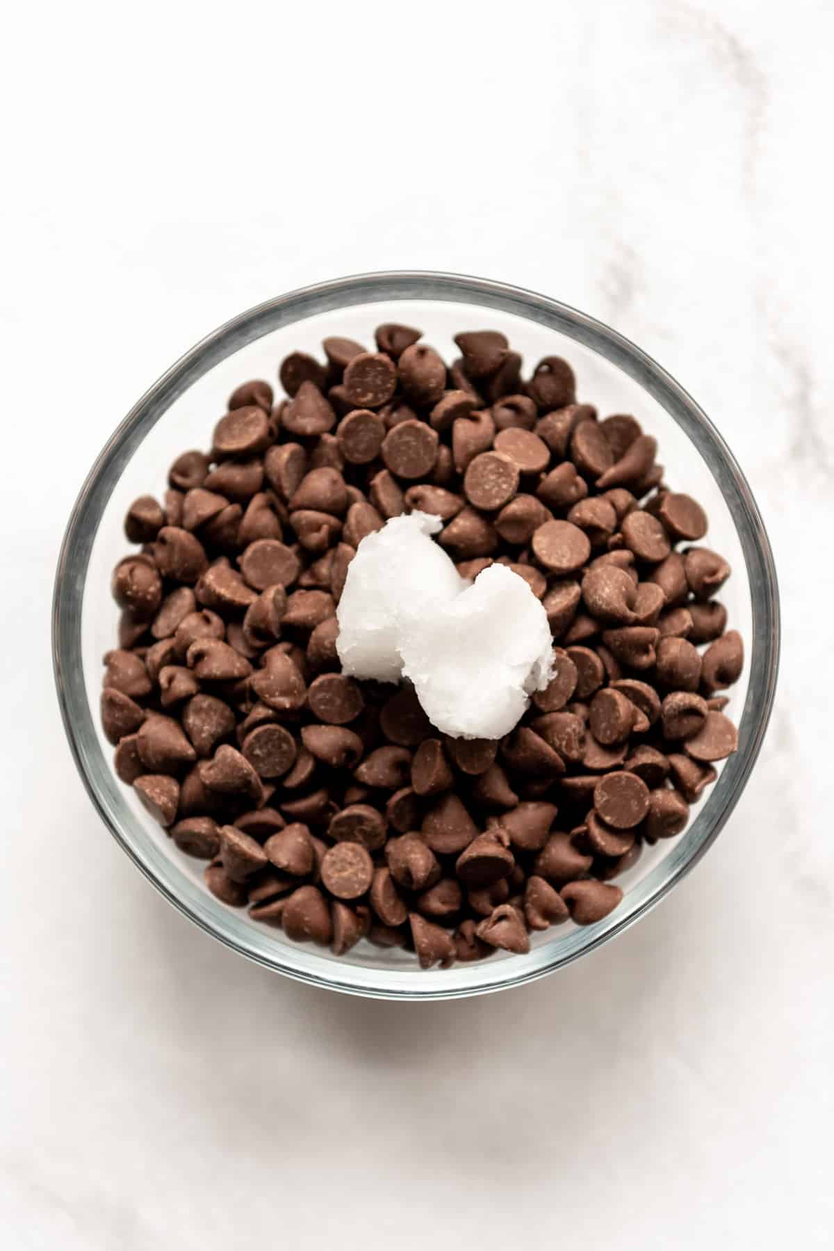 Chocolate chips in a glass bowl with coconut oil.