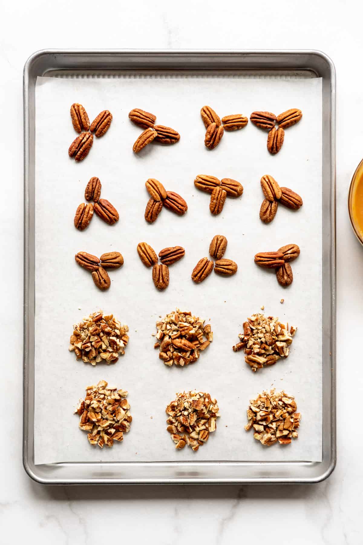 Piles of toasted whole or chopped pecans on a baking sheet.