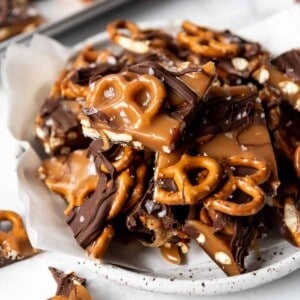 A plate piled with pieces of dark chocolate salted caramel pretzel bark.
