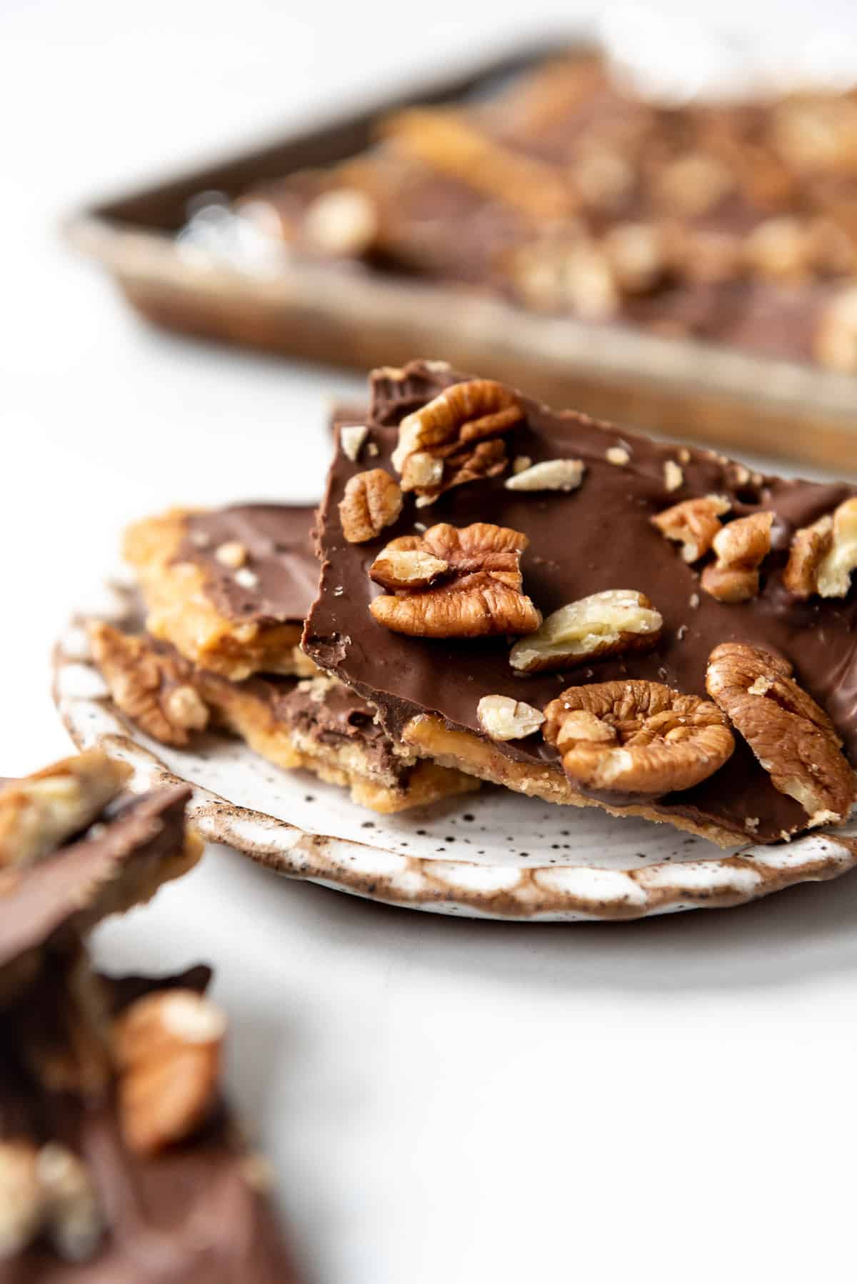 Pieces of saltine cracker toffee topped with chopped pecans on a plate.