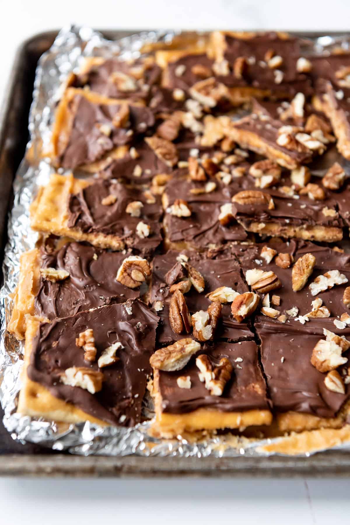 A pan of easy saltine cracker toffee with melted chocolate and chopped pecans on top.
