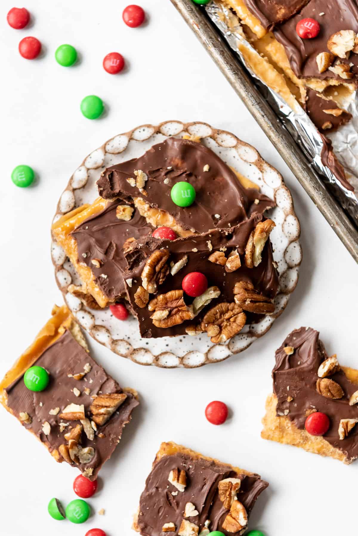 Pieces of saltine cracker toffee with red and green M&M's on a plate.