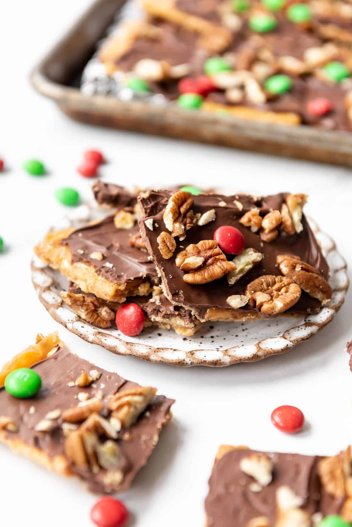Squares of homemade Christmas crack toffee with pecans and red and green M&M/s on a plate.