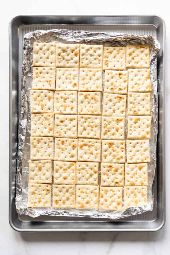 Saltine crackers arranged in a single layer on a baking sheet lined with aluminum foil for easy clean up.