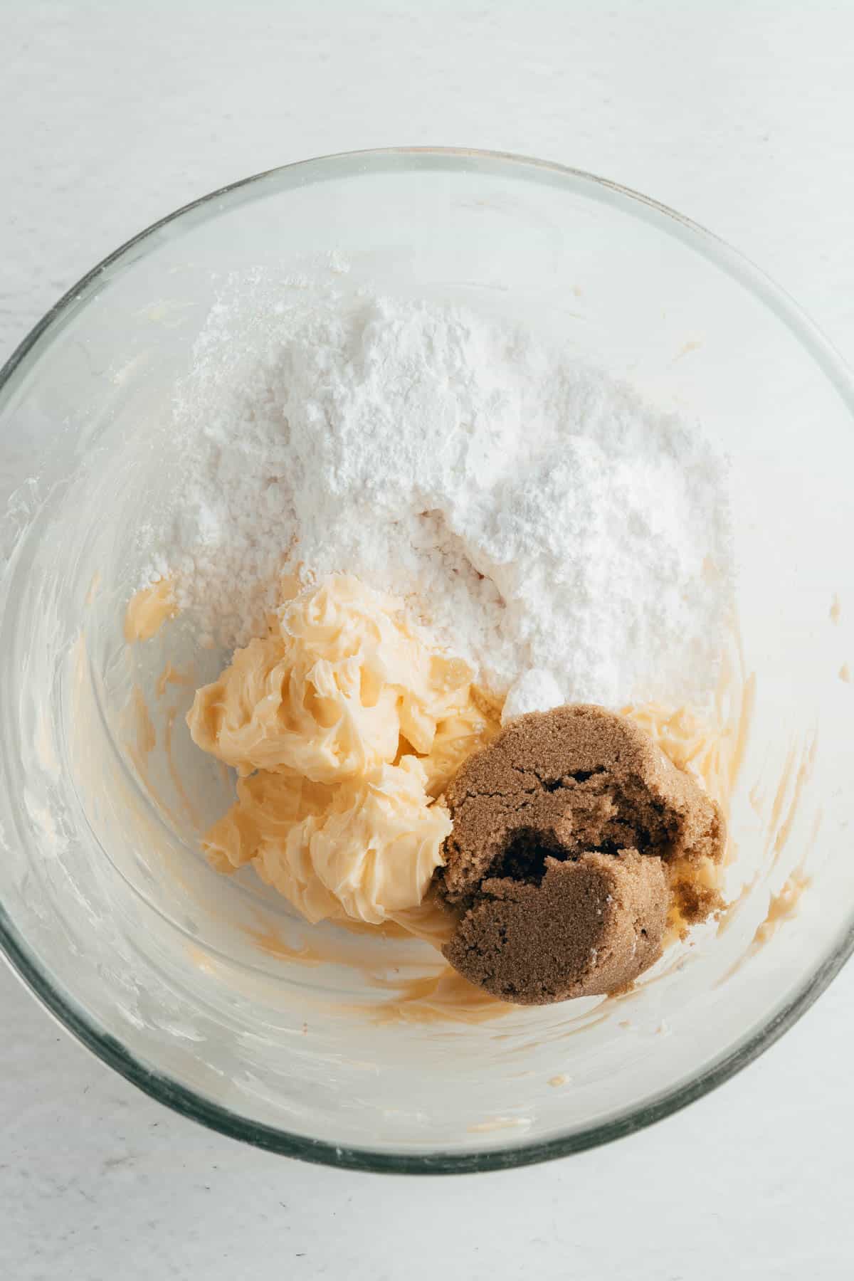 Powdered sugar, brown sugar, and softened butter in a glass mixing bowl.