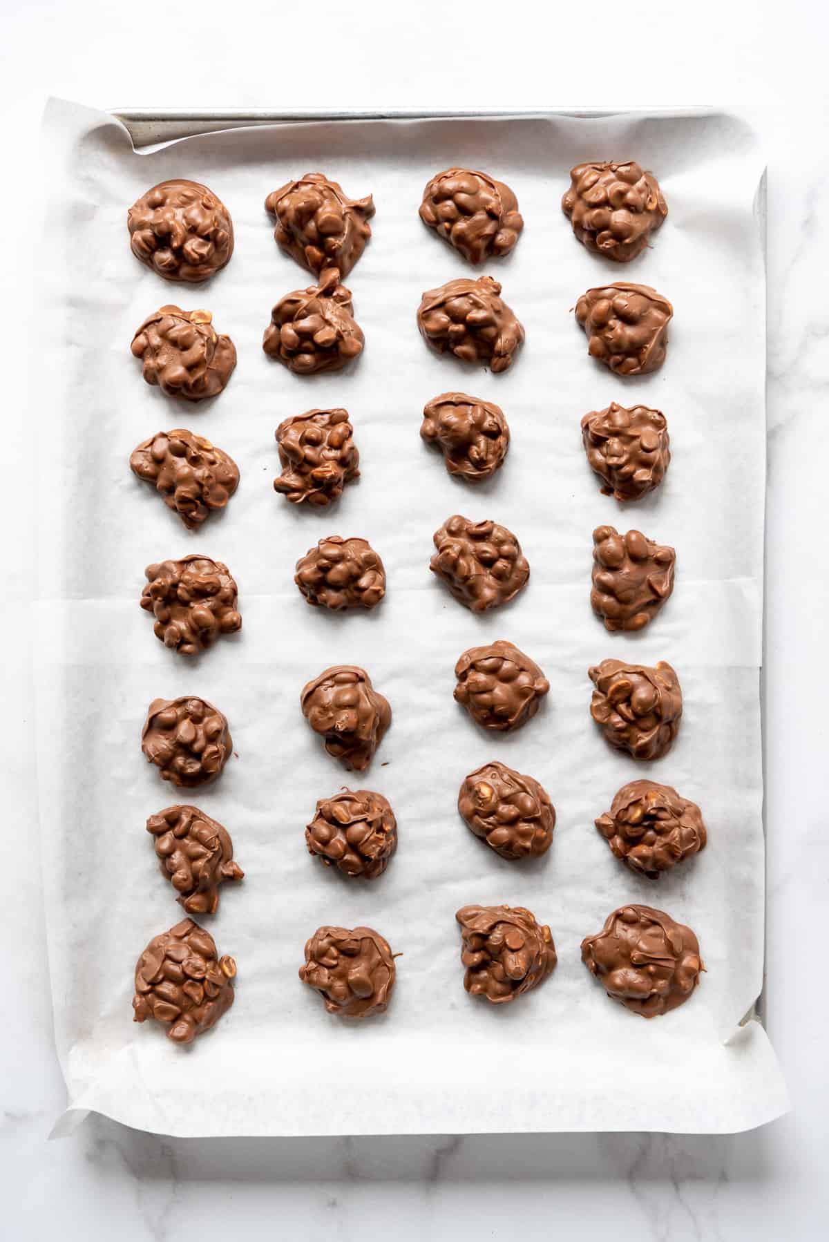 A large baking sheet lined with parchment paper filled with peanut clusters candy made in the crockpot.
