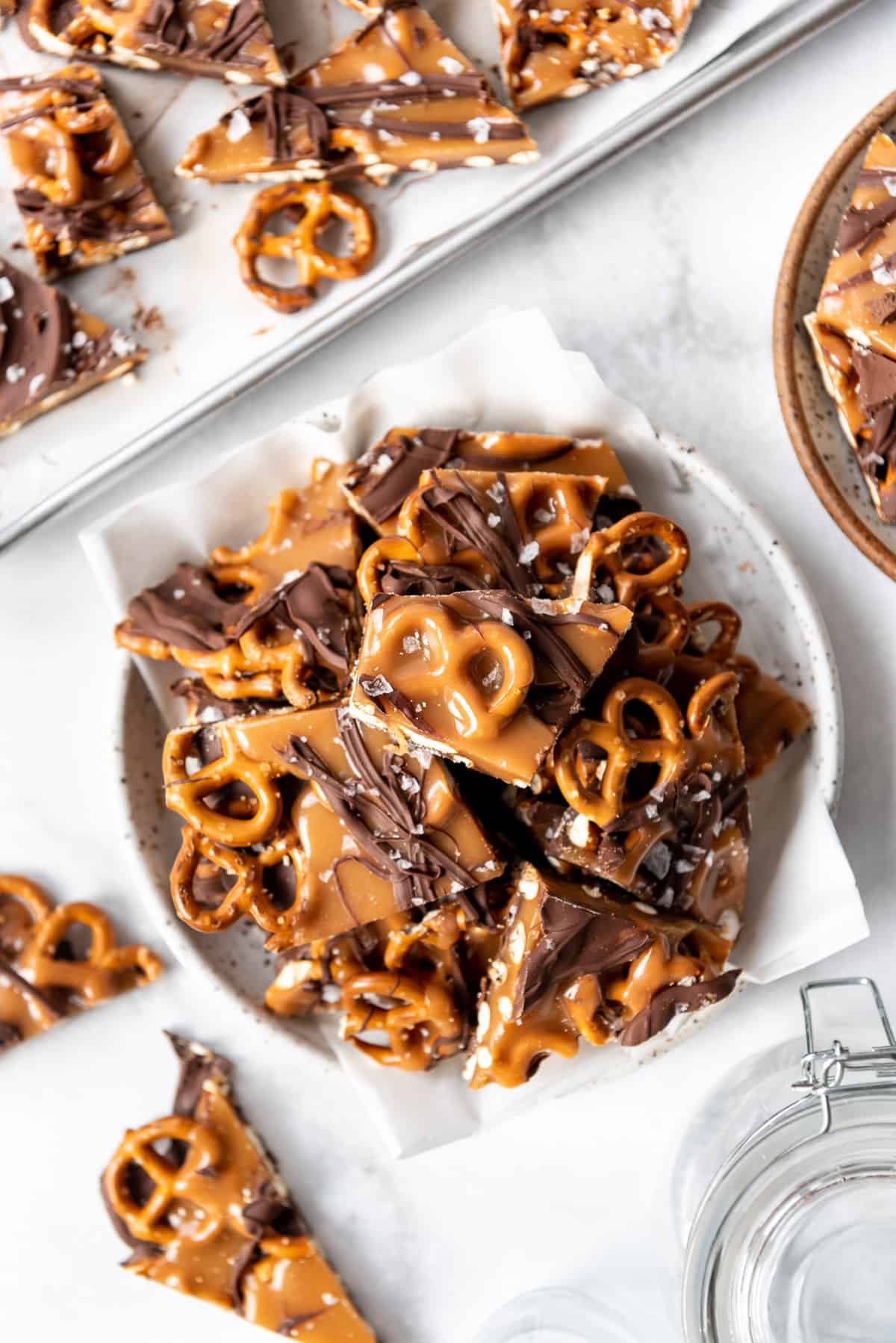 A plate full of dark chocolate salted caramel pretzel candy sprinkled with flaky Maldon salt on top.