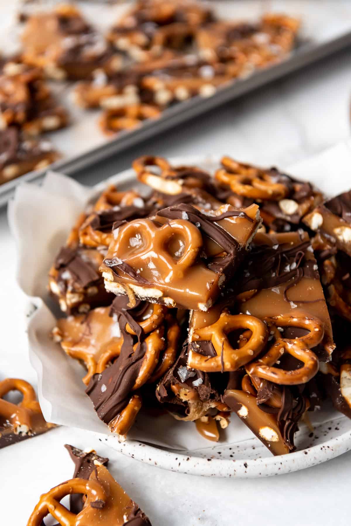 Squares of crunchy and chewy salted caramel pretzel candy with chocolate drizzled on top.