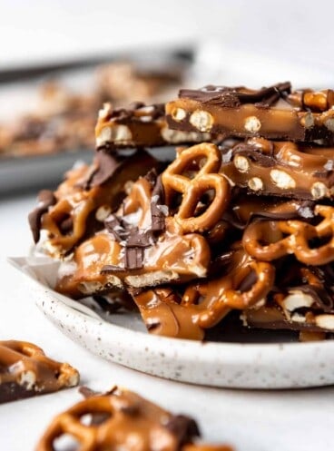 A plate piled with pieces of homemade dark chocolate salted caramel pretzel bark.