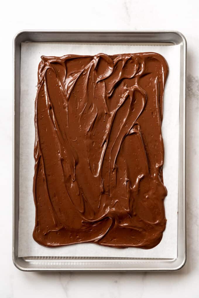 Melted semisweet chocolate spread in a layer on a baking sheet lined with parchment paper.