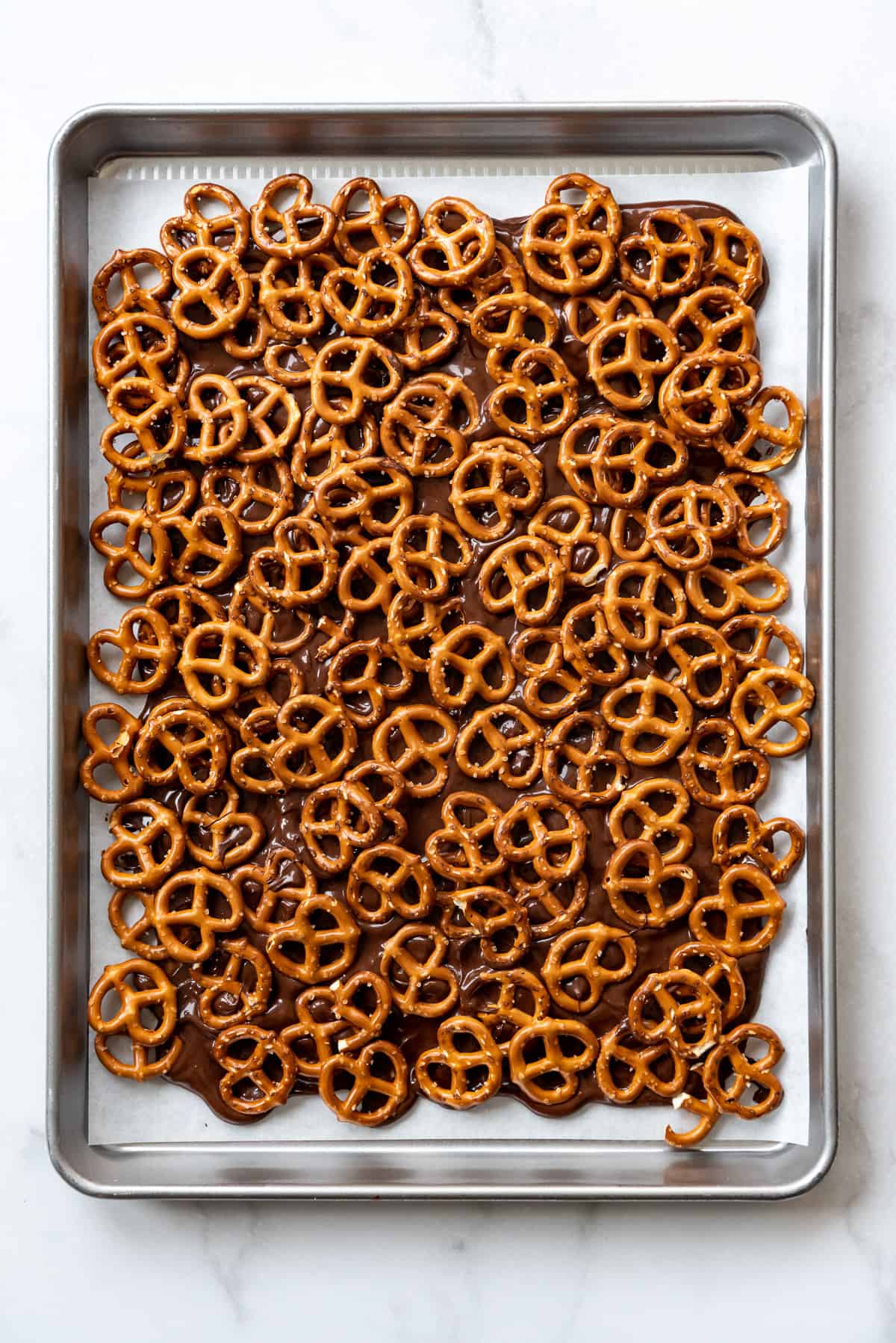 Dark chocolate and pretzels on a parchment paper lined baking sheet.