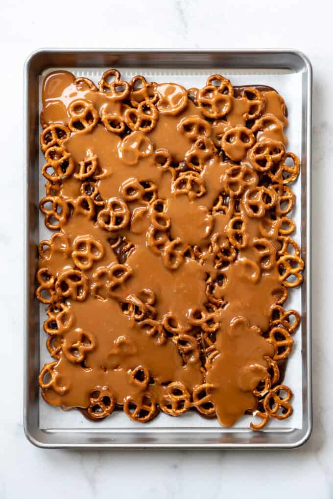 Caramel poured over layers of pretzels and dark chocolate on a parchment paper lined baking sheet.