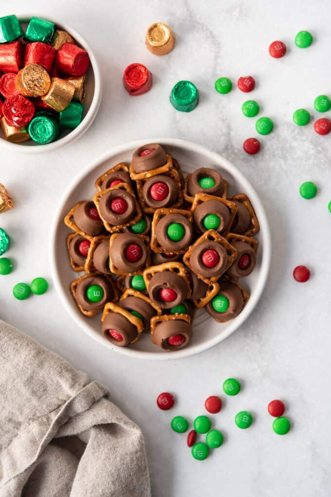 A white plate with red and green Christmas M&Ms topped easy Rolo pretzels candy.