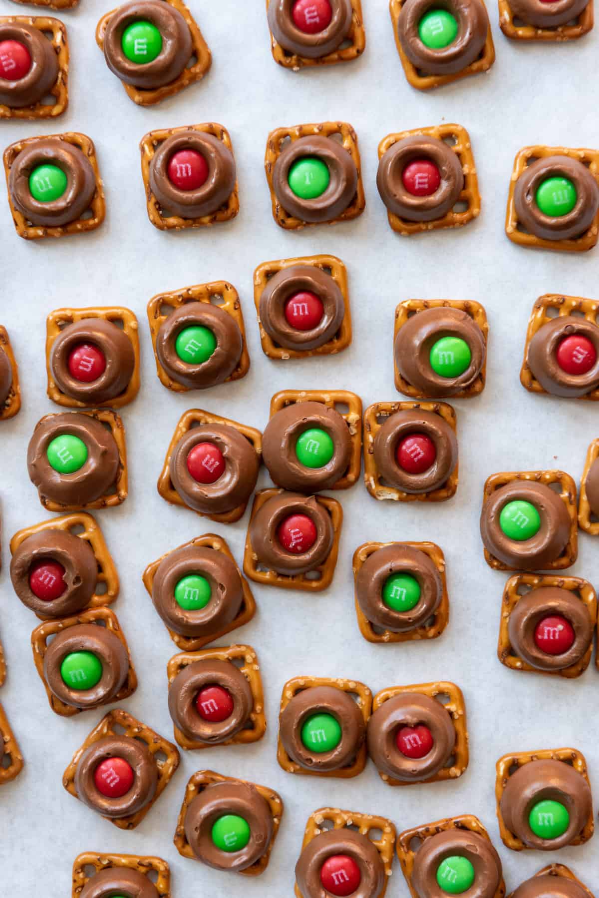 Christmas Rolo pretzels made with M&Ms scattered on a parchment paper surface.