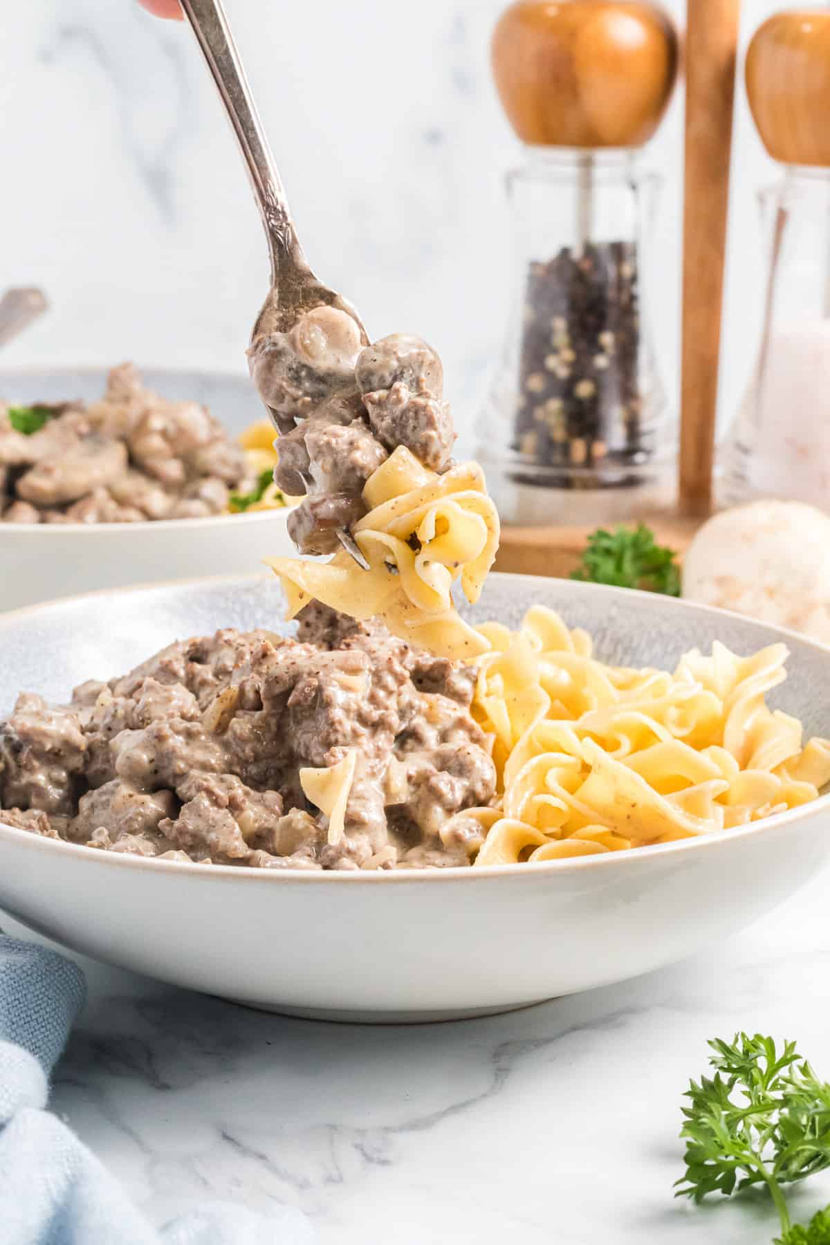 A fork lifting a bite of egg noodles with ground beef stroganoff.