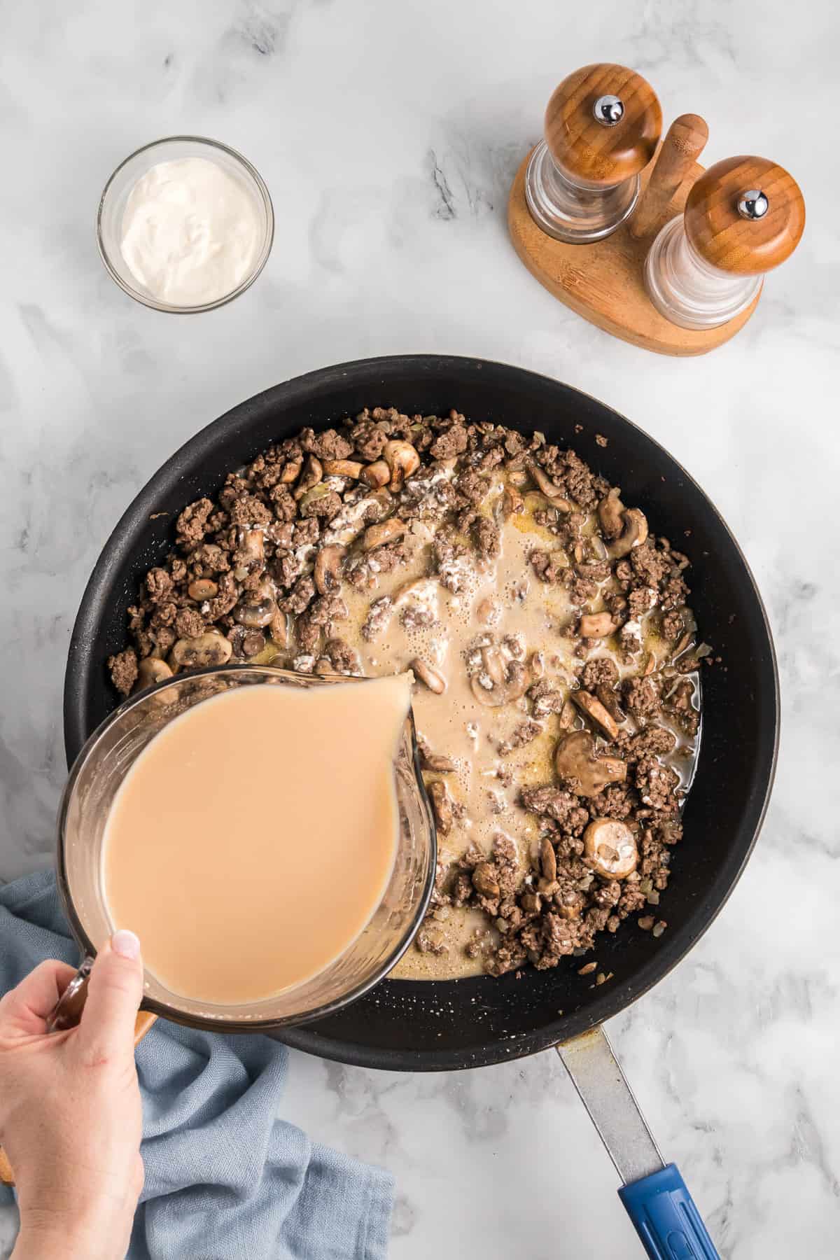 Adding beef broth mixed with flour to ground beef and mushrooms in a pan.