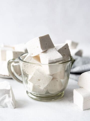 Homemade marshmallow cubes in a glass measuring cup.