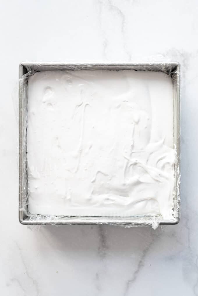 Freshly made marshmallow poured into a square baking dish lined with plastic wrap.