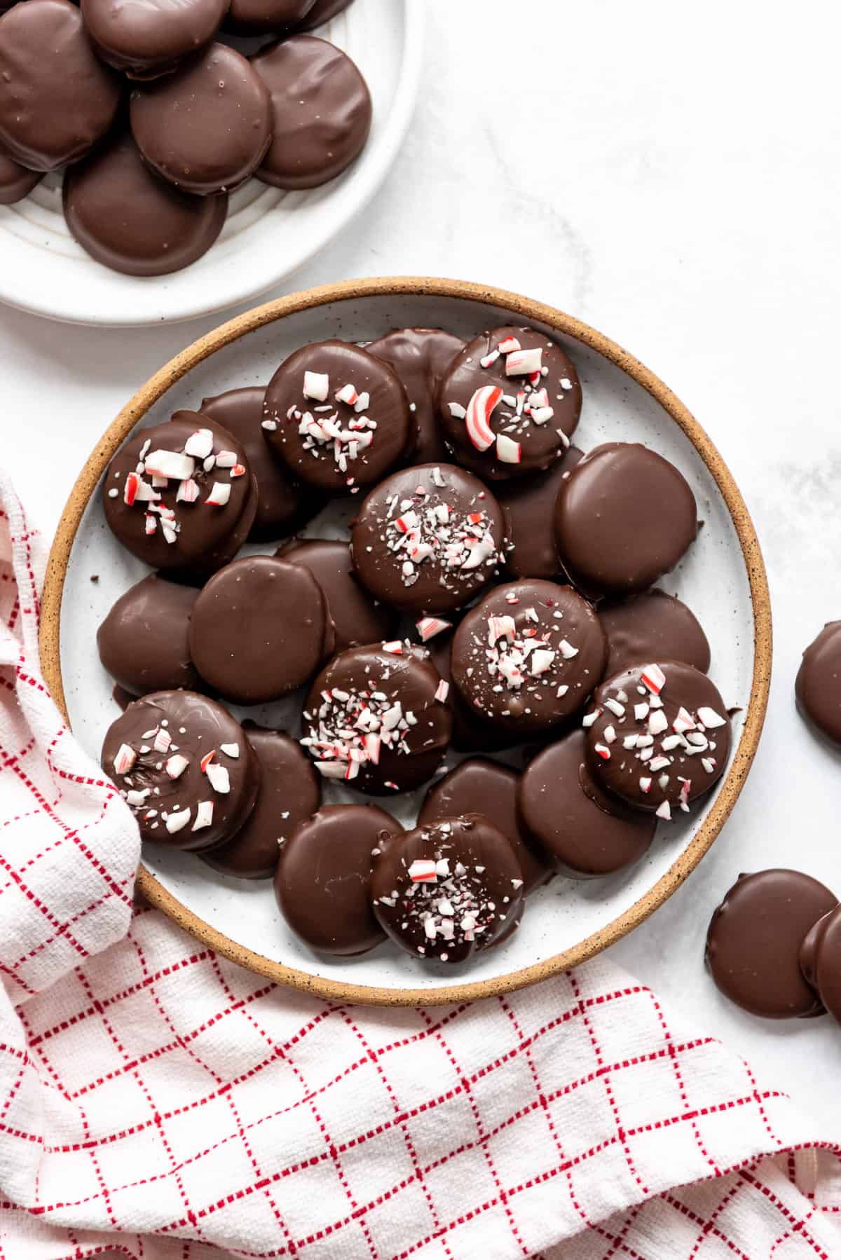 A plate of homemade peppermint patties decorated with dark chocolate and crushed candy cane pieces.