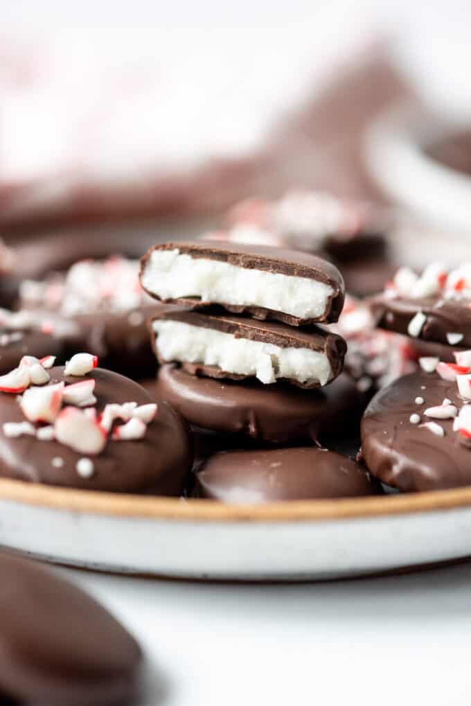 Two halves of a homemade peppermint patty stacked on a plate with other peppermint patties around sprinkled with crushed candy cane pieces.