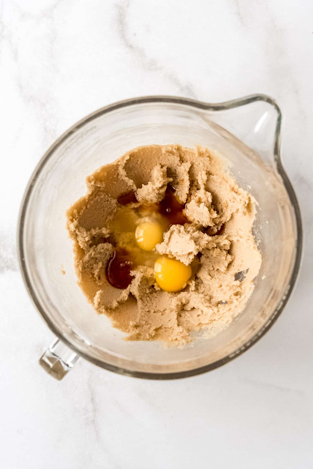 Adding eggs and vanilla to creamed butter and sugar in a glass bowl.