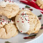 Three thick peanut butter cookies with white chocolate chips dipped in white chocolate with Christmas sprinkles on a plate.