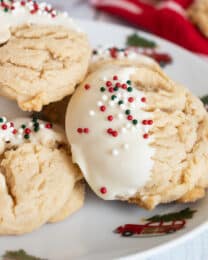 Three thick peanut butter cookies with white chocolate chips dipped in white chocolate with Christmas sprinkles on a plate.