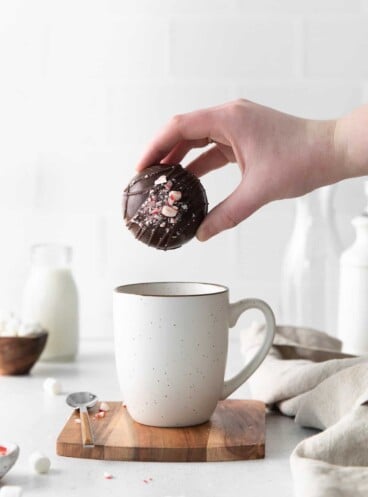 A hand dropping a peppermint hot cocoa bomb into a white mug.