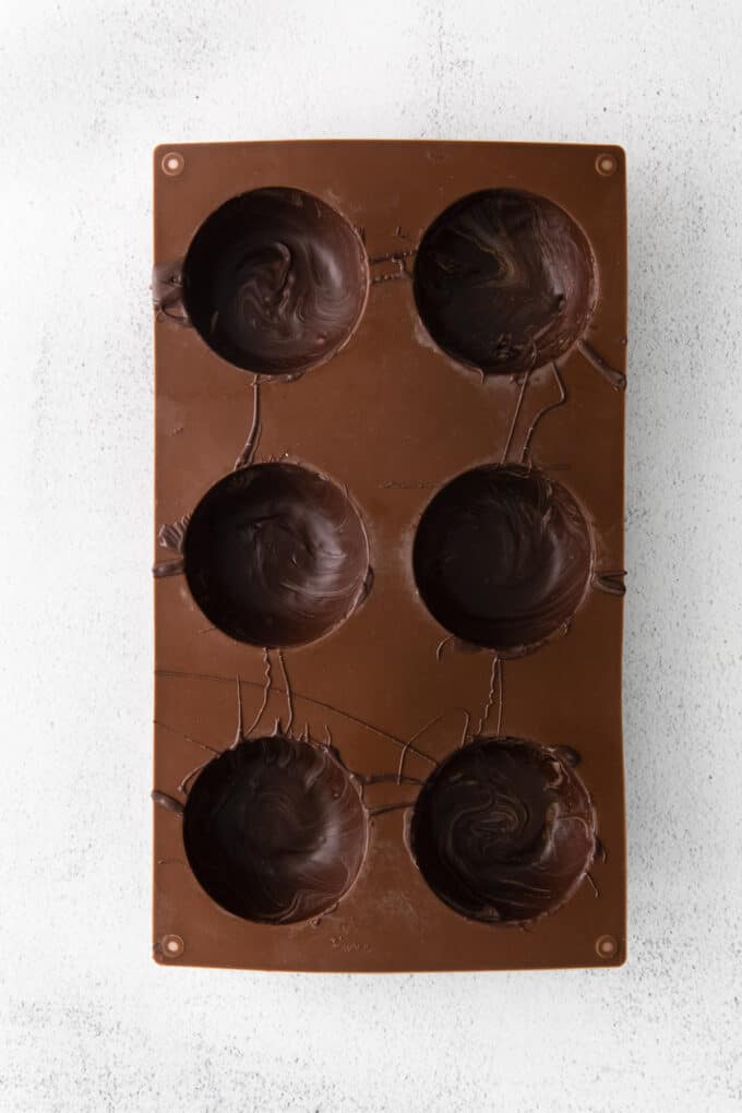 Chocolate brushed into a silicone mold for making hot cocoa bombs.