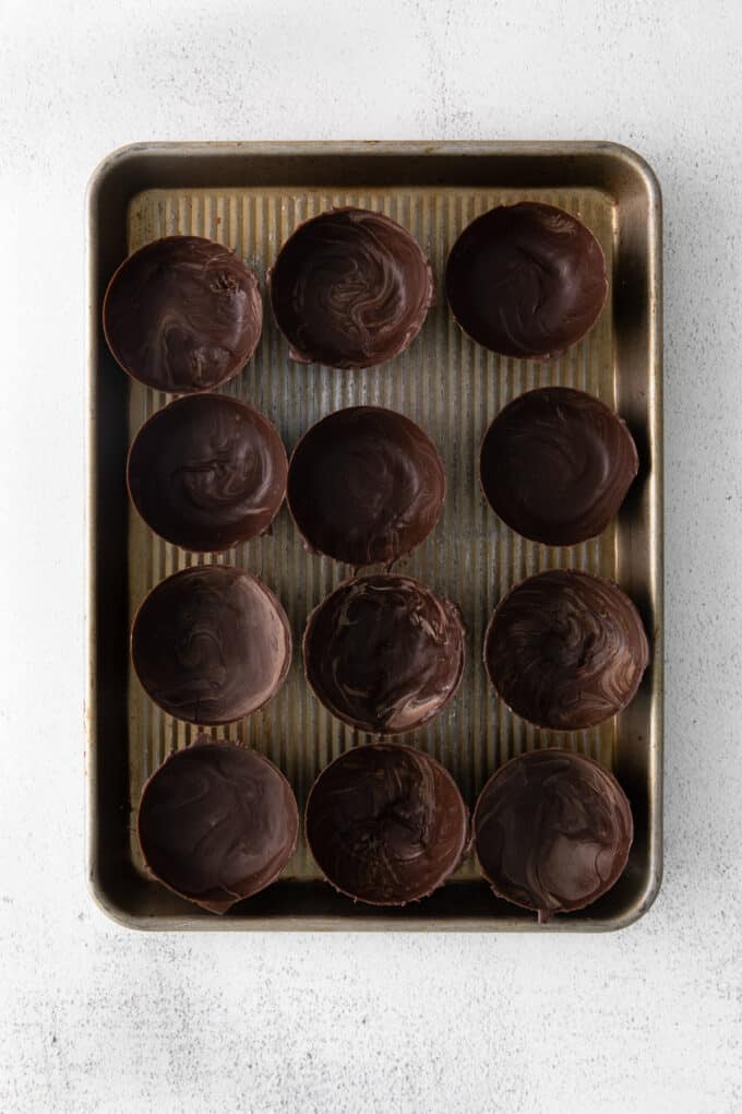 Unmolded chocolate dome halves for making hot cocoa bombs on a baking sheet.