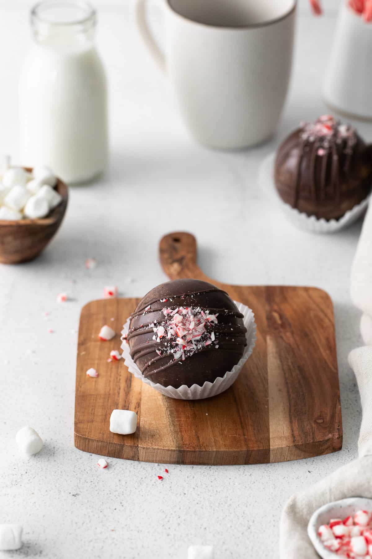A homemade hot chocolate bomb decorated with crushed candy canes in a white cupcake liner on a wooden cutting board.