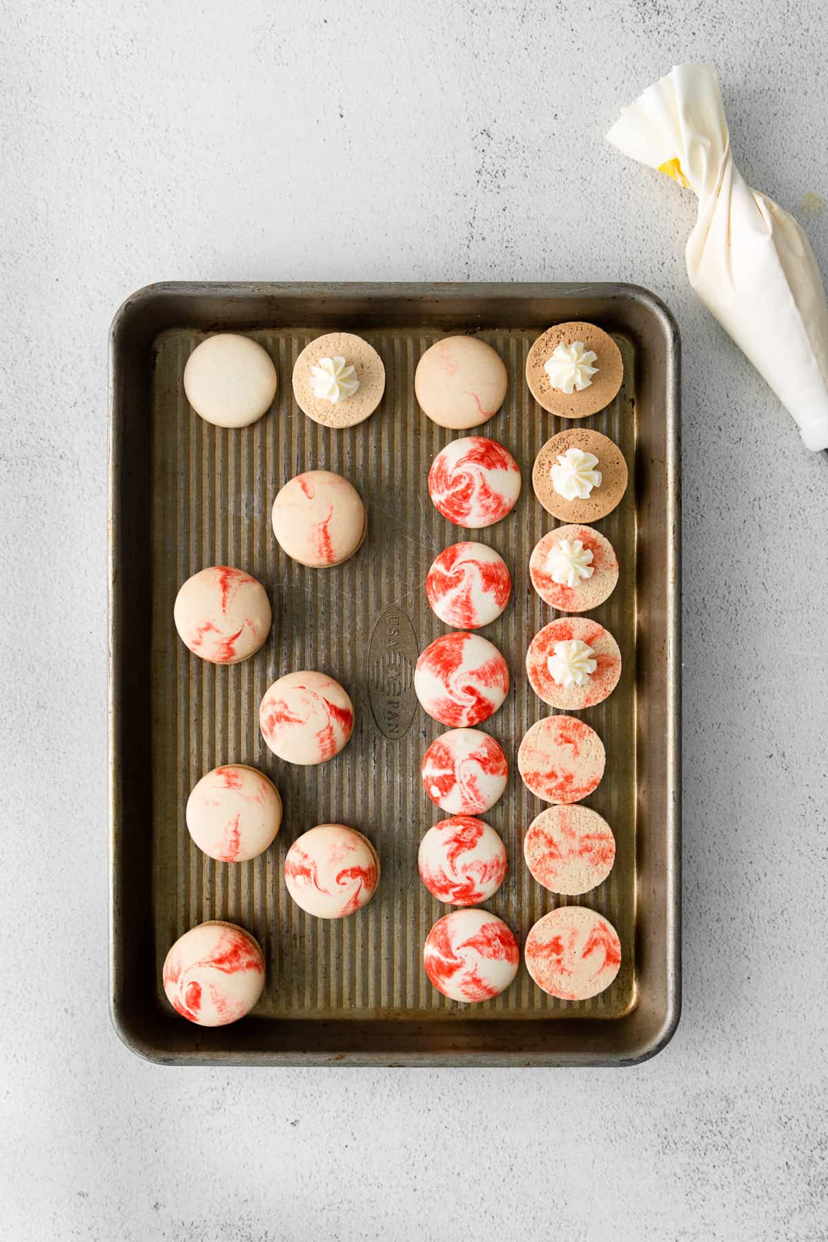 Piping peppermint buttercream onto red and white swirled macaron shells.