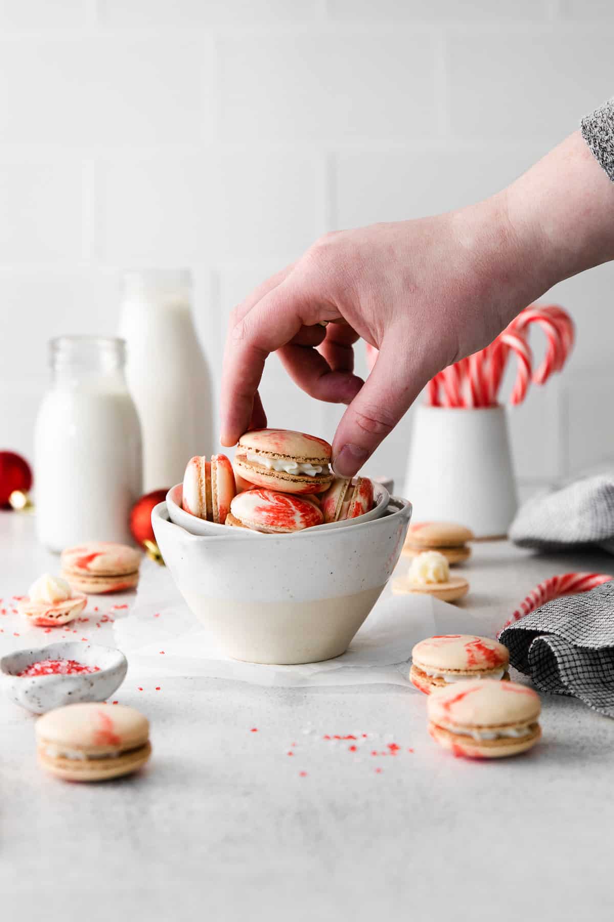A hand reaching to pick up a peppermint macaron from a bowl.