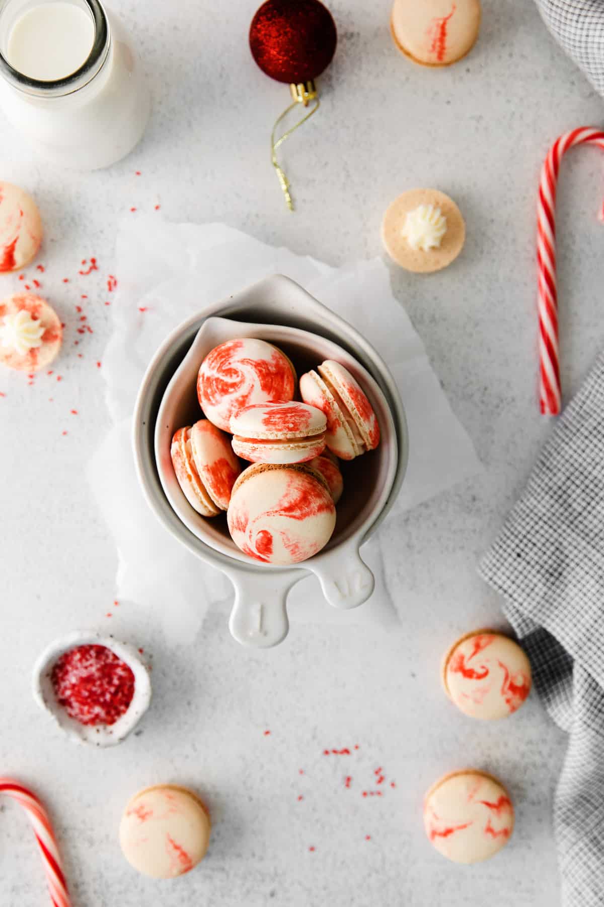 An overhead image of peppermint macarons scattered with candy canes, sprinkles, and ornaments.