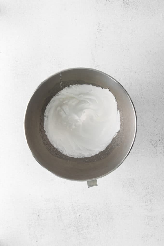 Egg whites beaten to stiff peaks with sugar in a mixing bowl.