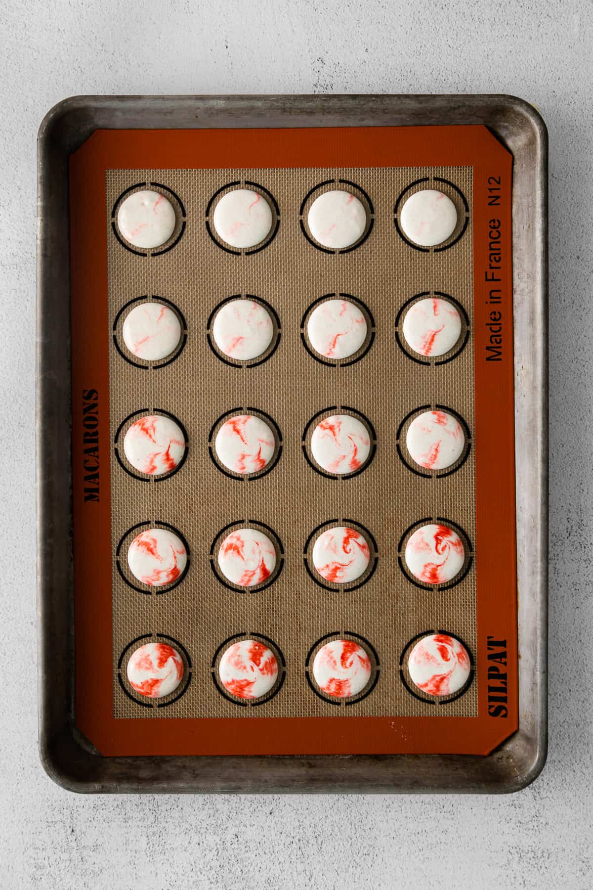 Piped peppermint macaron shells on a silicon mat.