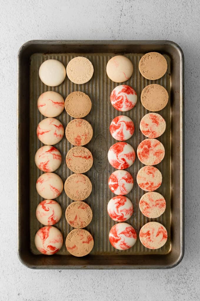 Baked peppermint macaron shells that have been matched up with half turned upside down on a baking sheet.