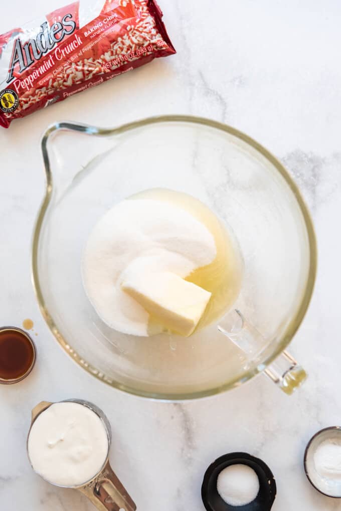 A large glass mixing bowl with granulated sugar, softened butter, and oil.