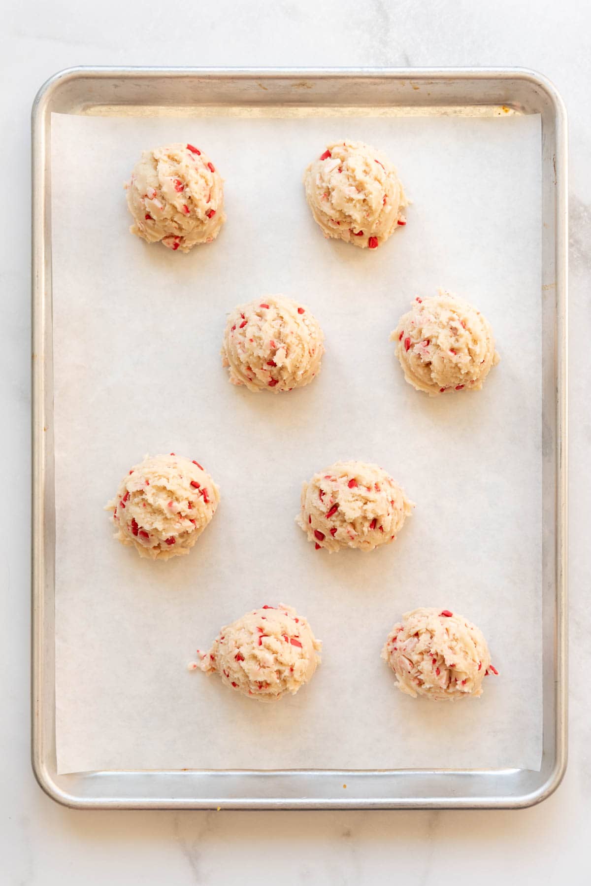 An overhead image of unbaked balls of cookie dough on a baking sheet lined with parchment paper.