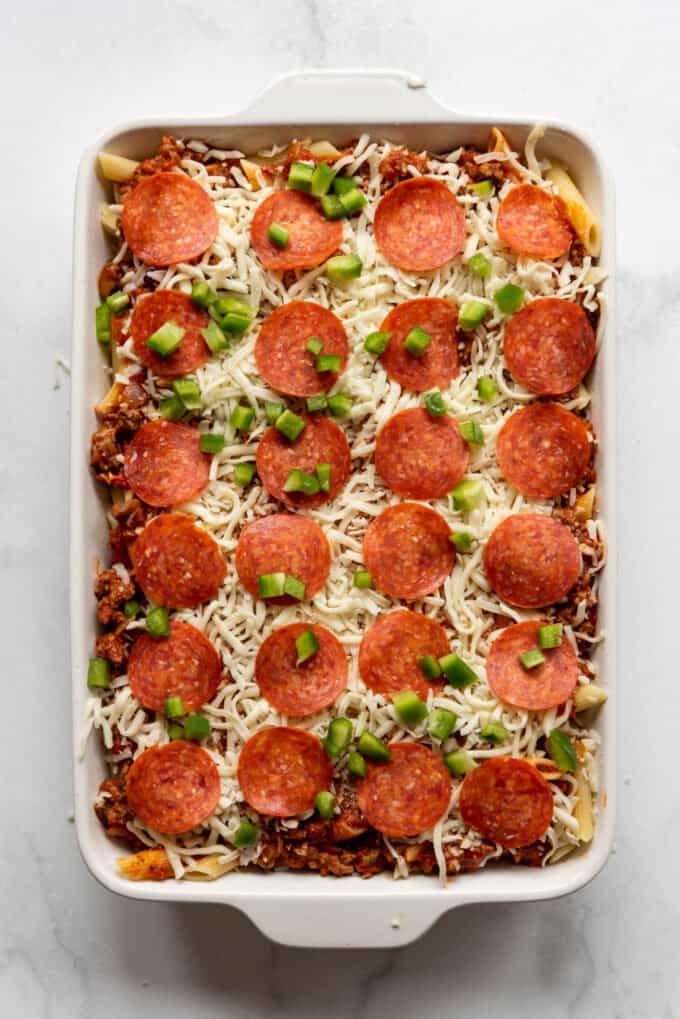 Topping a pizza casserole with pepperoni and green bell pepper.