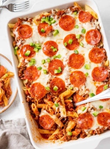 A large casserole dish of pizza casserole with a serving spoon scooping some out.