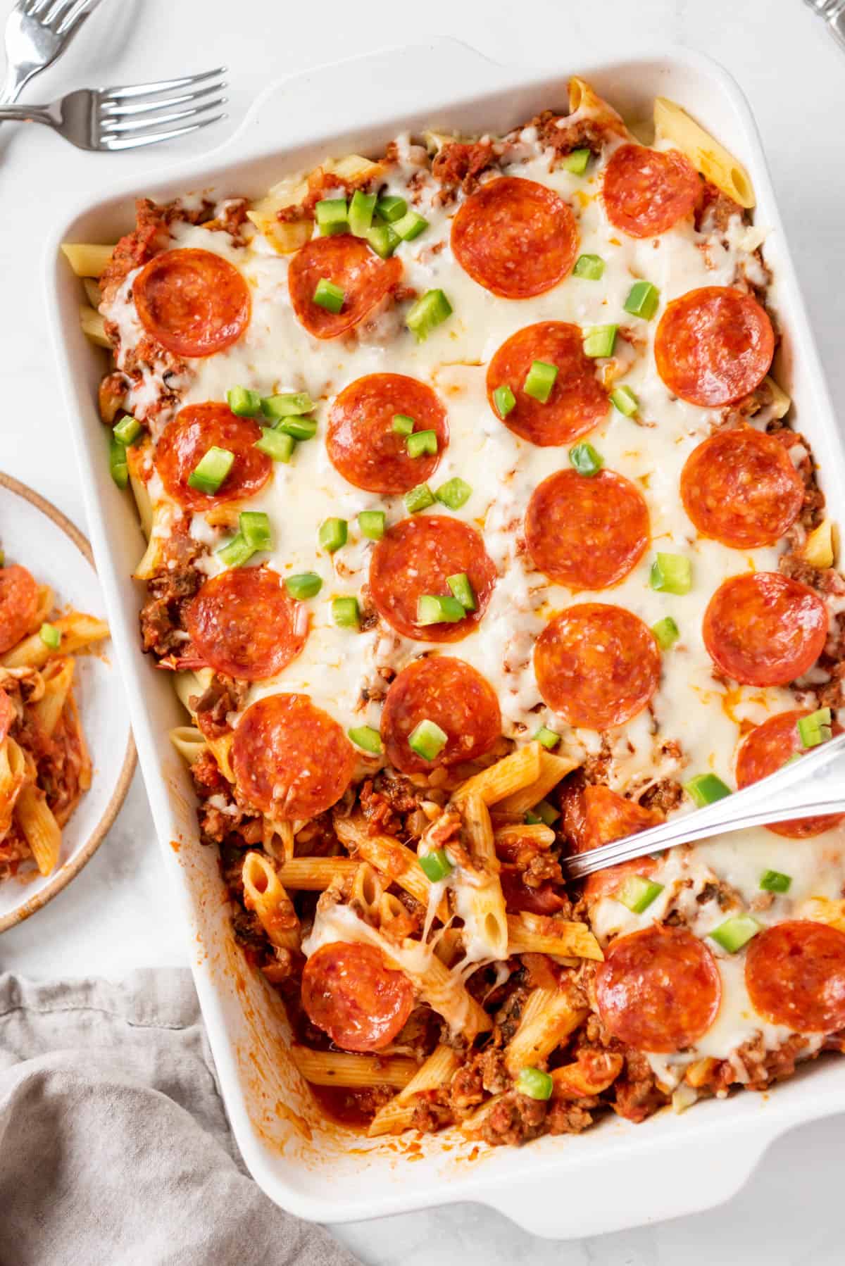 A large casserole dish of pizza casserole with a serving spoon scooping some out.